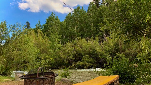 A rustic outdoor setting with a metal fire pit and a wooden bench. - Kenosha Lodge (Grant)