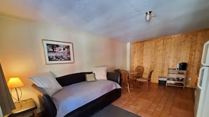 A cozy room with a bed, a small table with chairs, a lamp, and a wooden wall. - Kenosha Lodge (Grant)