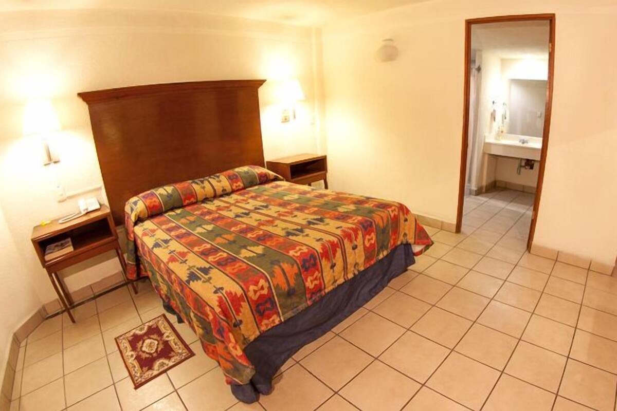 Un dormitorio con cama, mesitas de noche, una alfombra y un baño visible a través de una puerta abierta.