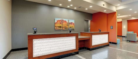 A reception area with two wooden reception desks, a patterned wall, and a painting of a desert landscape.