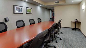Un salón de conferencias con una larga mesa de madera, seis sillas de oficina negras, dos cuadros en la pared y una pequeña mesa con un teléfono y un objeto decorativo.