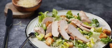 A plate of sliced meat with croutons and lettuce on a dark surface.