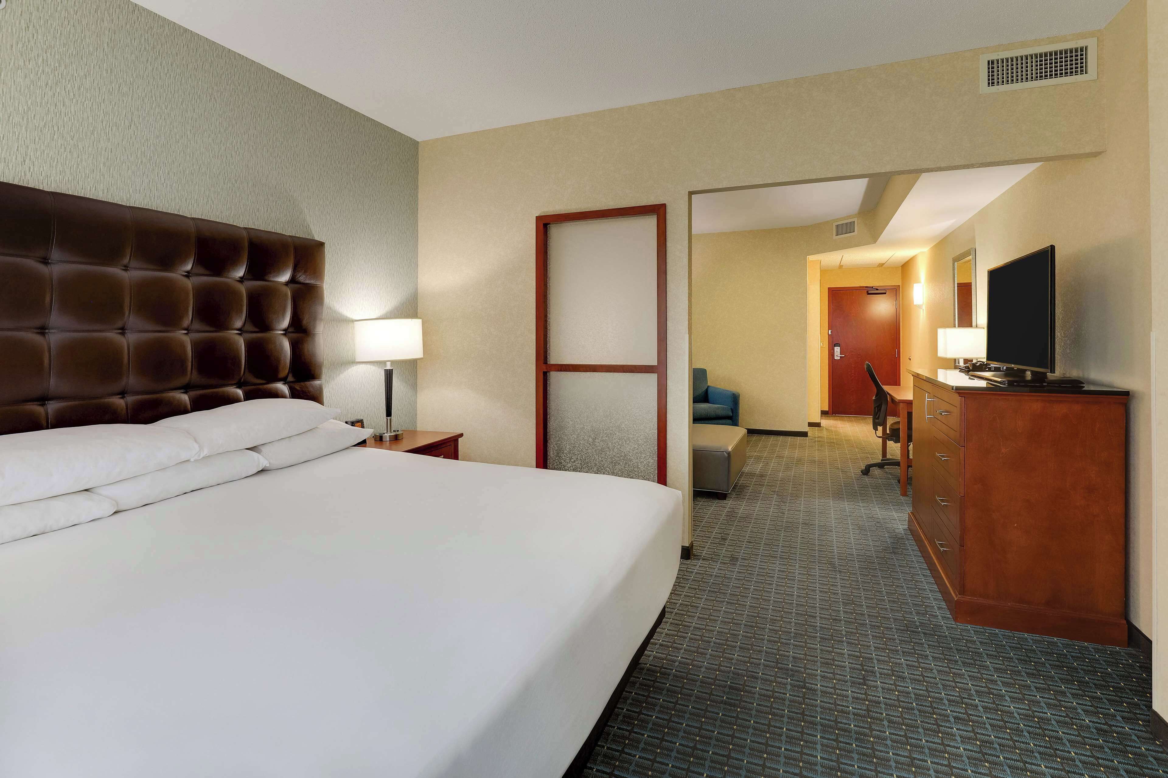 Quarto de hotel com uma cama grande, uma escrivaninha com computador, televisão e guarda-roupa.