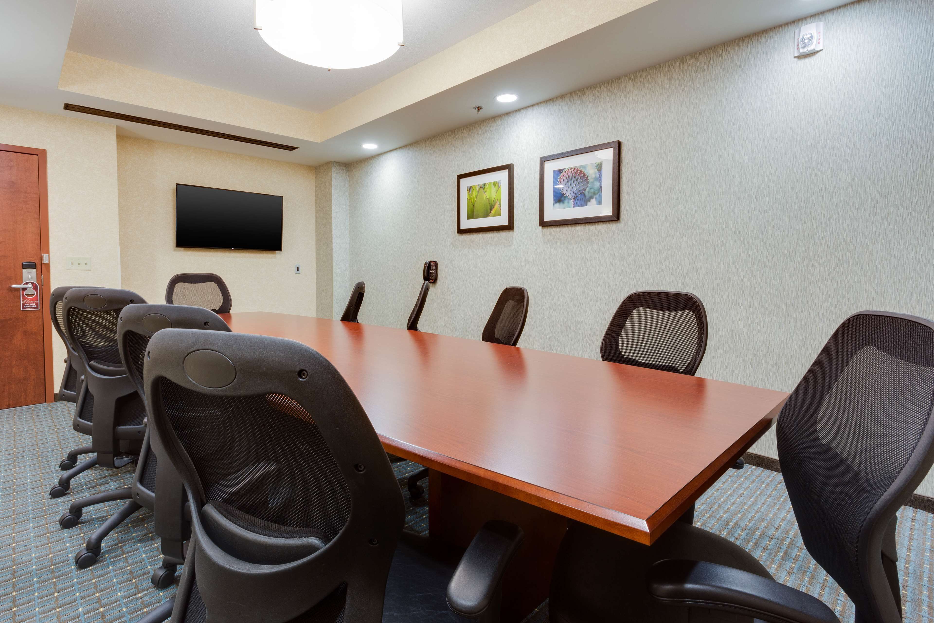 A conference room with a long table, six chairs, a flat-screen TV, and two framed pictures on the wall.
