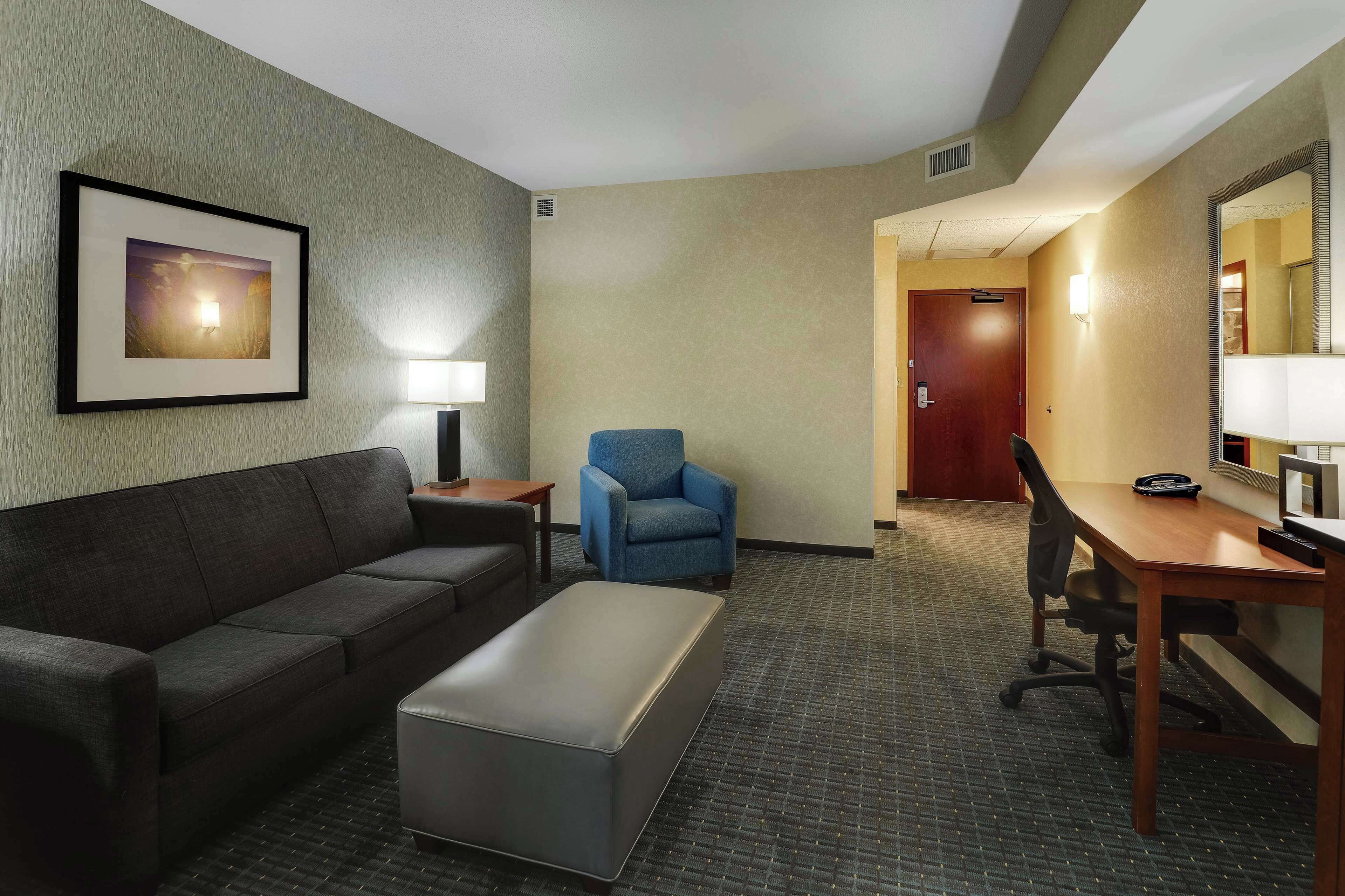 A hotel room with a sofa, armchair, desk, and a framed picture on the wall.