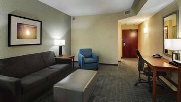 A hotel room with a sofa, armchair, desk, and a framed picture on the wall.
