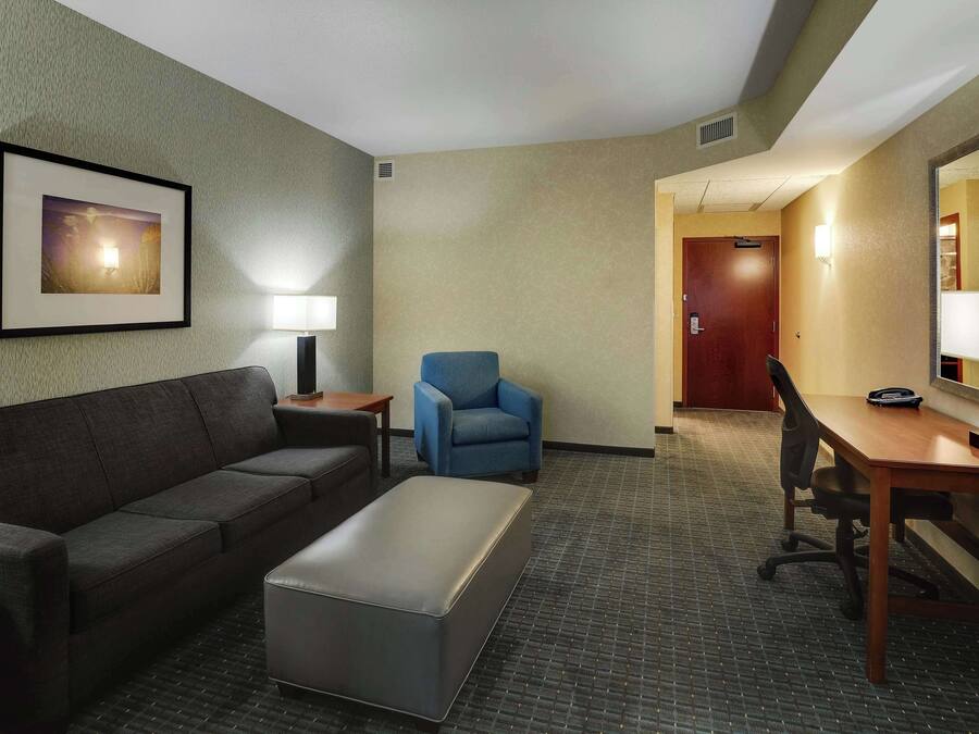 A hotel room with a sofa, armchair, desk, and a framed picture on the wall.