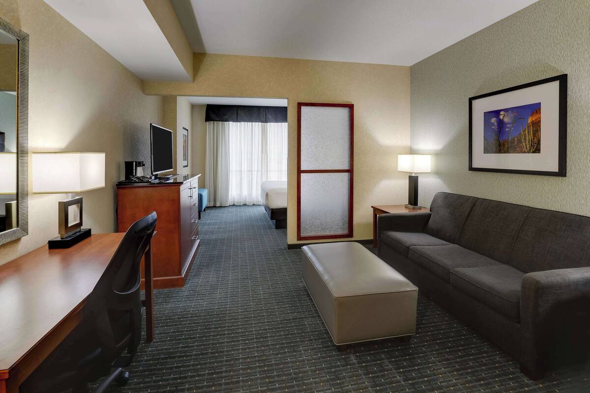 Ein Hotelzimmer mit Schreibtisch, einer Couch, einem Fernseher, einer Lampe und einem gerahmten Bild an der Wand.