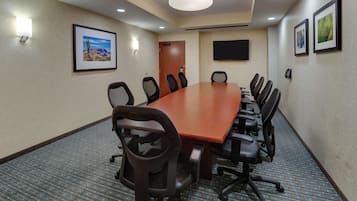 A conference room with a long table, multiple chairs, a door, framed pictures, and a flat-screen TV.