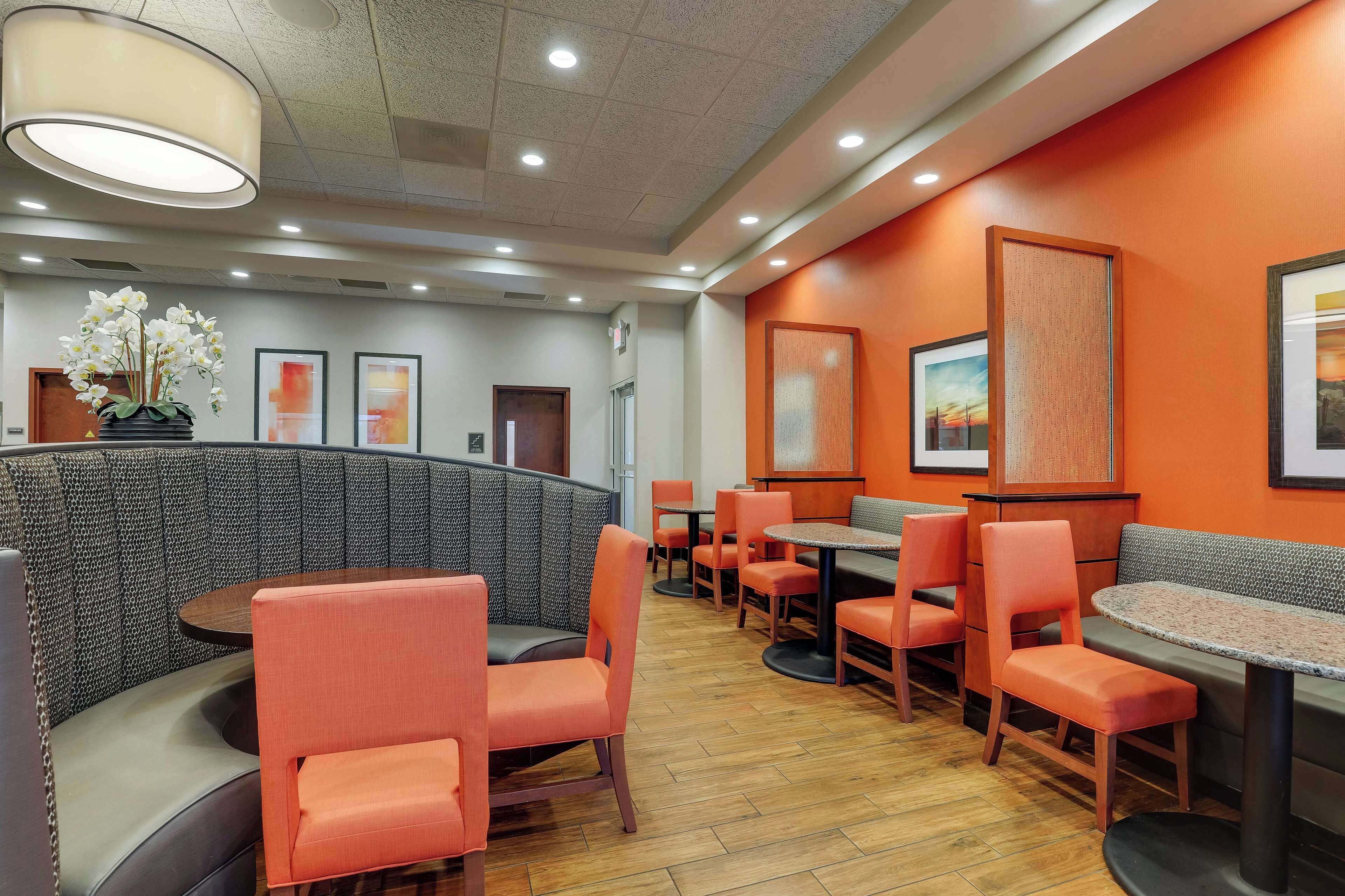 Un restaurant avec des banquettes et des tables, des chaises orange et des œuvres d’art accrochées aux murs.