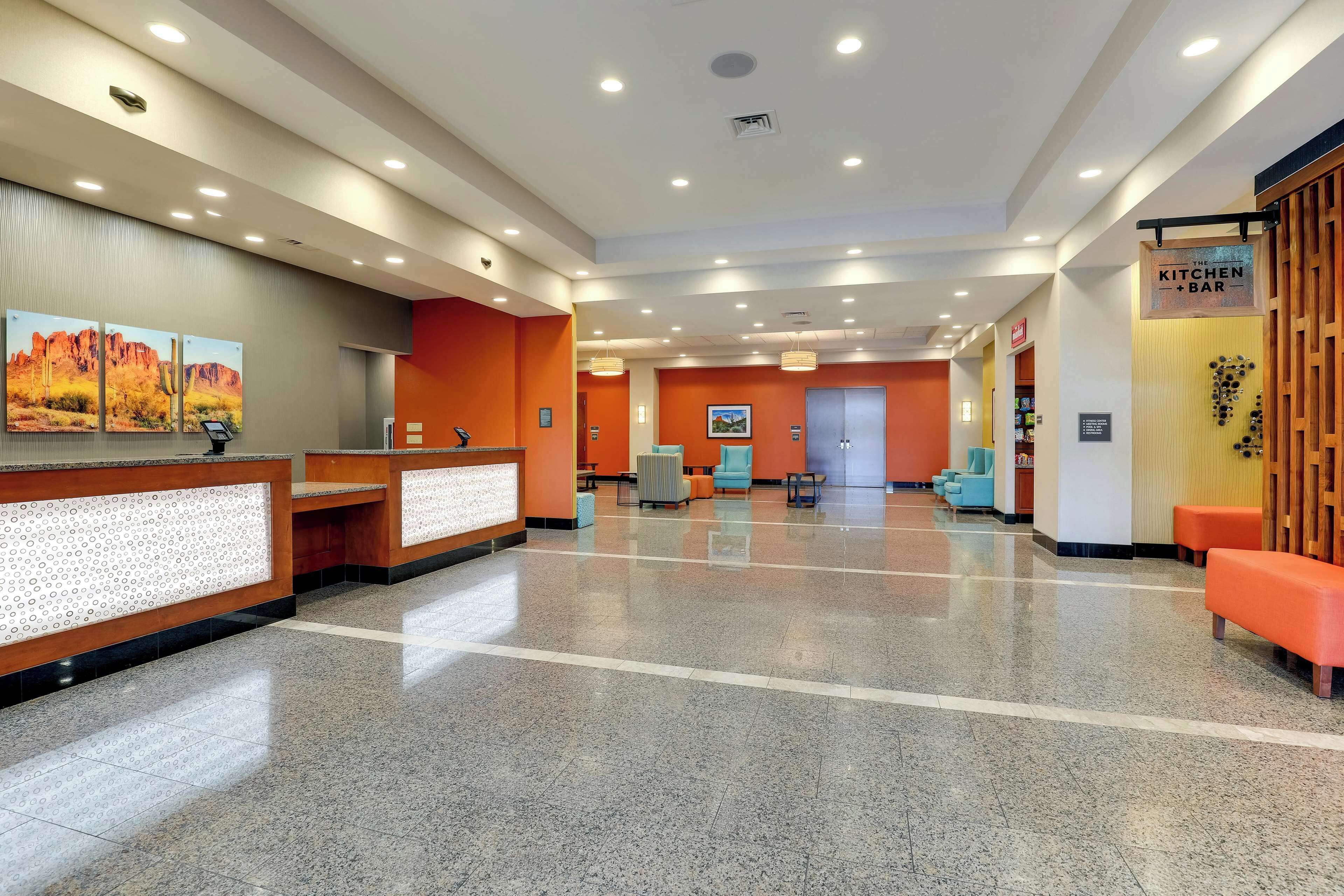 A hotel lobby with a reception desk, seating area, and a sign for 'The Kitchen Bar'.