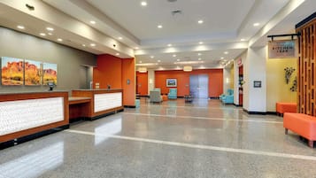 A hotel lobby with a reception desk, seating area, and a sign for 'The Kitchen Bar'.