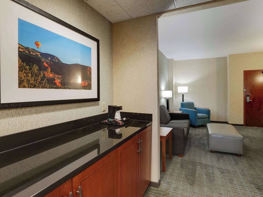 A hotel lobby with a black counter, a framed picture of a hot air balloon, a blue armchair, a gray sofa, and a wooden door.