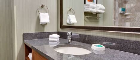 A bathroom with a granite countertop sink, a mirror, and a towel rack with folded towels.