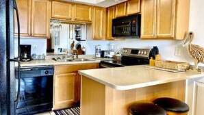 A modern kitchen with wooden cabinets, a black refrigerator, a microwave, a stove, and a sink. - SunSwept 505 by ALBVR (Orange Beach)