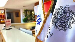 A reception area with a white counter, a sign reading "Welcome", and two flags with emblems. - Telemly Hotel (Algiers)