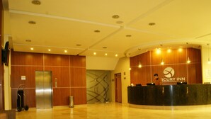 A Mercury Inn reception area with a wooden reception desk, a digital screen, and a luggage cart. - Hotel Mercury Inn (Querétaro)