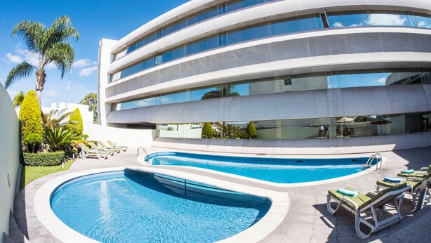 A modern building with a pool area, including two swimming pools and lounge chairs. - Hotel Mercury Inn (Querétaro)