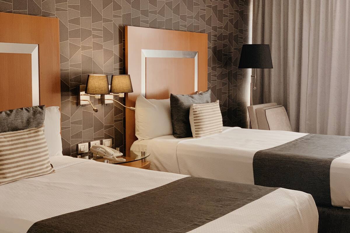 A hotel room with two beds, a nightstand with a lamp, and a telephone.