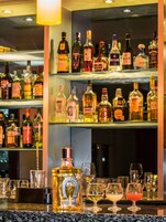 Zona de bar con varias botellas de licores y vasos en estantes.