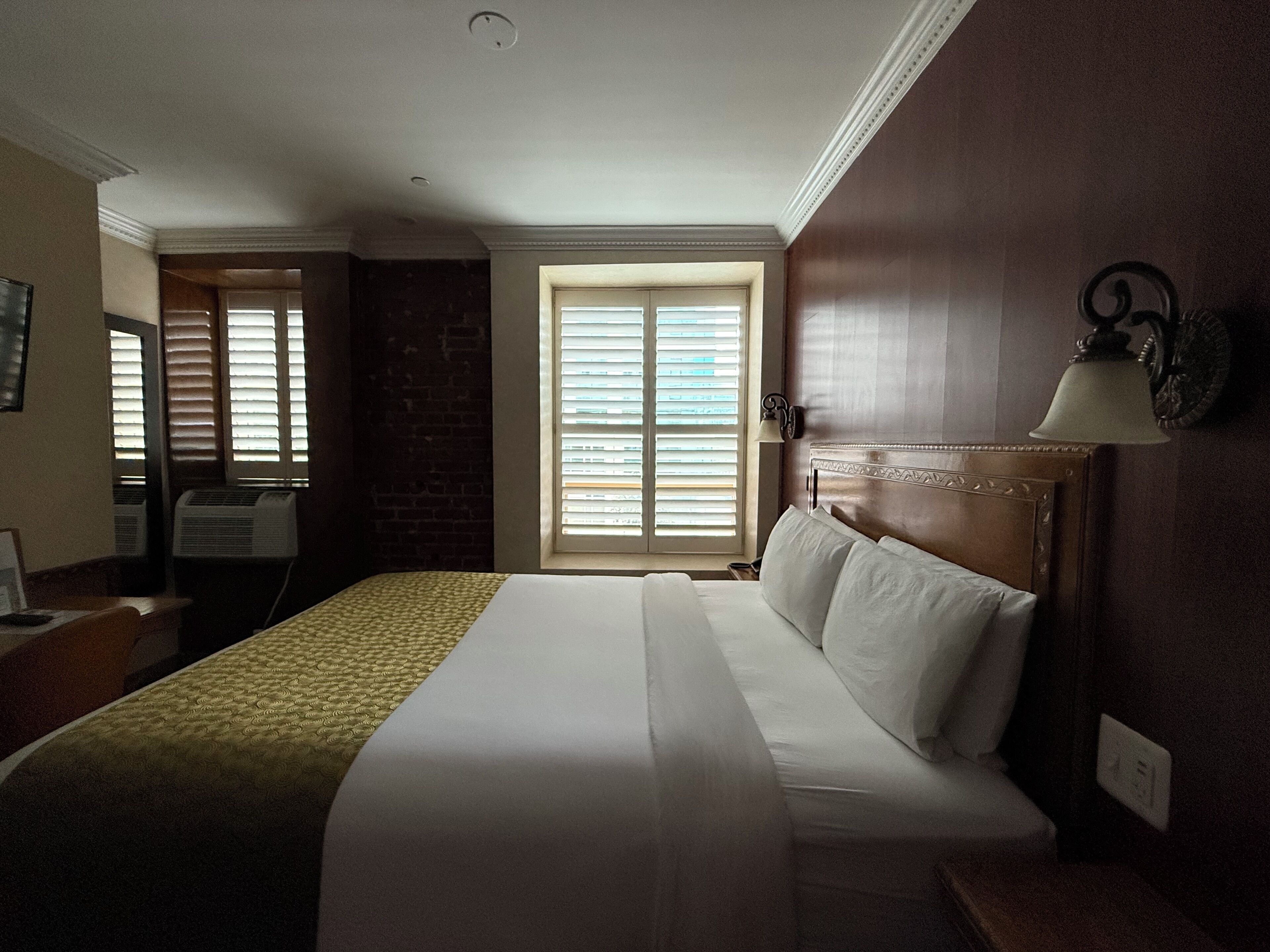 A hotel room with a large bed, a desk, a chair, and a window with blinds.