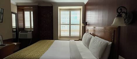 A hotel room with a large bed, a desk, a chair, and a window with blinds.