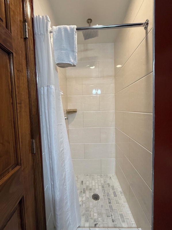 A shower with beige tiles, a wooden door, and a white shower curtain. - The Architect (Washington)