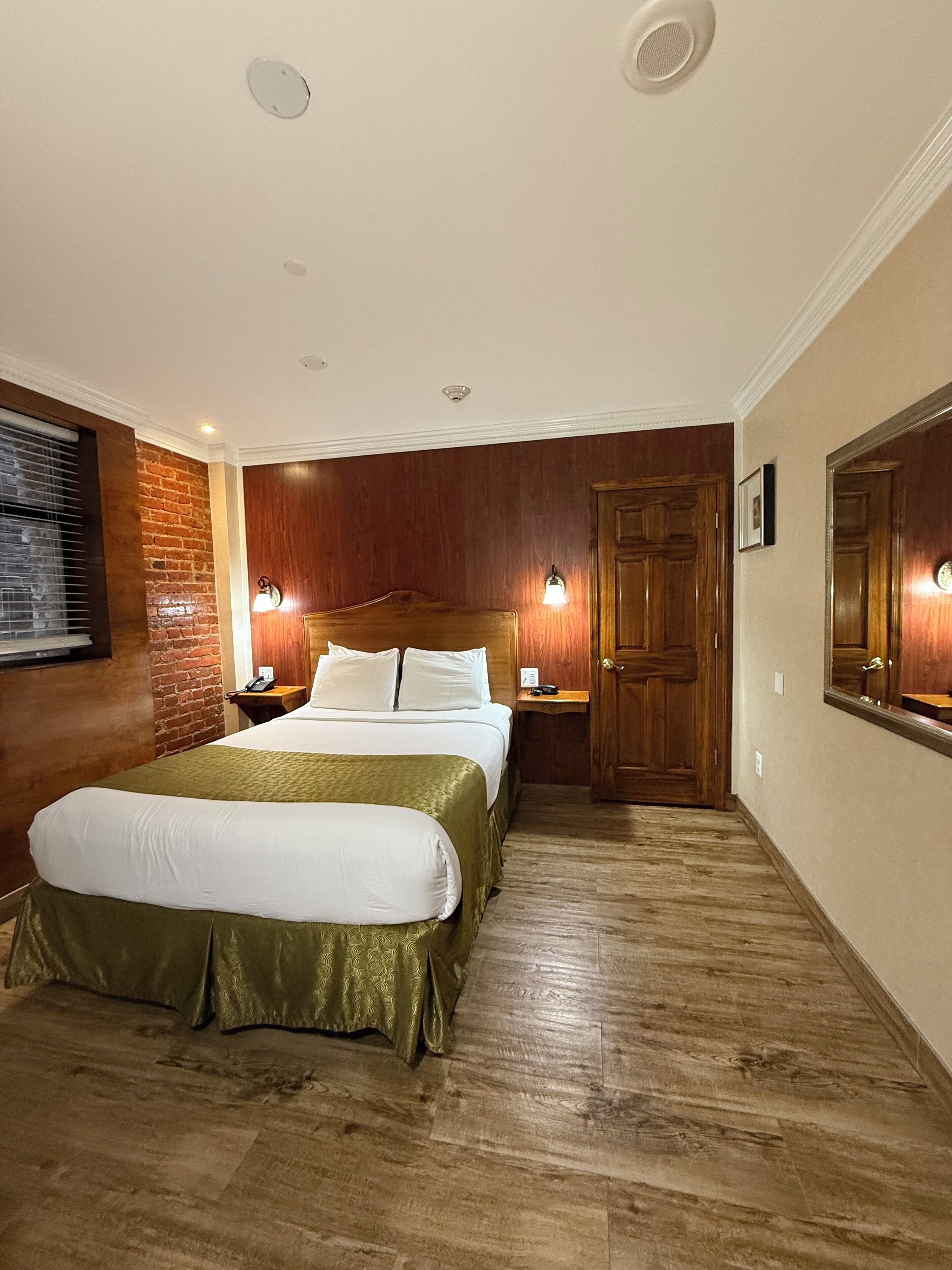 Une chambre d’hôtel avec un grand lit, des lambris en bois aux murs, une porte en bois et une petite table de chevet avec une lampe.