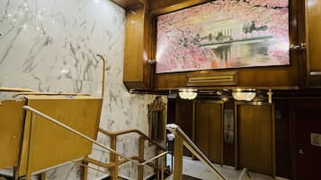 Un vaste hall d’entrée aux murs de marbre, orné d’un grand lustre et d’un tableau représentant un cerisier en fleurs.