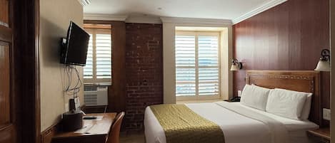 Habitación de hotel con cama, escritorio, silla, televisión y ventana con persianas.