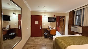 A hotel room with a large mirror, a desk with a chair, a bed, and a television.