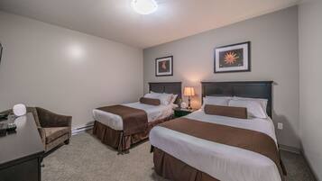 A hotel room with two beds, a desk, a chair, and a lamp.
