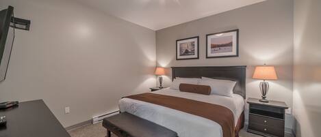 Una habitación de hotel con una cama, mesitas de noche con lámparas, un banco, un escritorio y una lámpara en el techo.