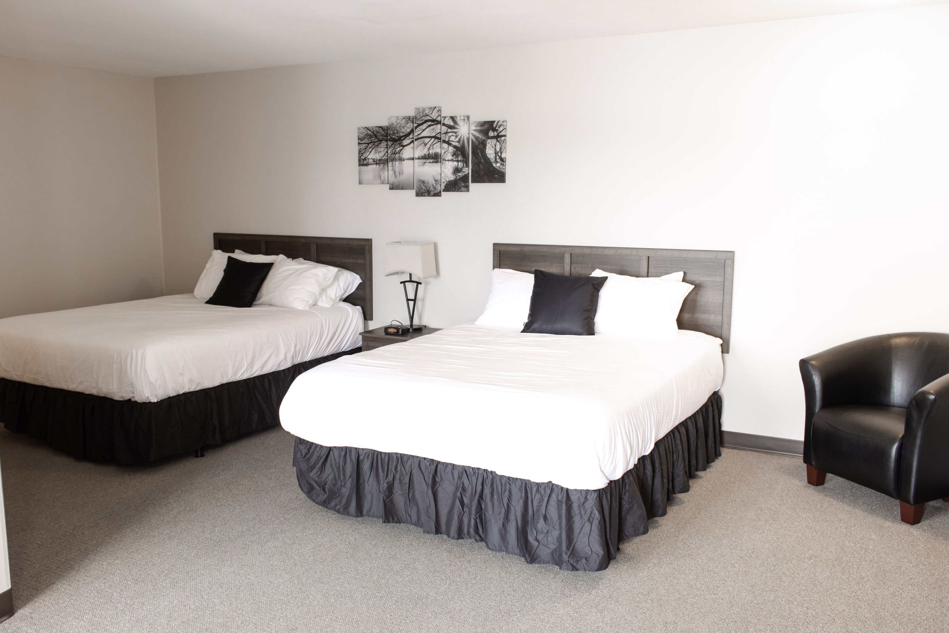 Two single beds with dark headboards, a black leather armchair, and a wall-mounted lamp.