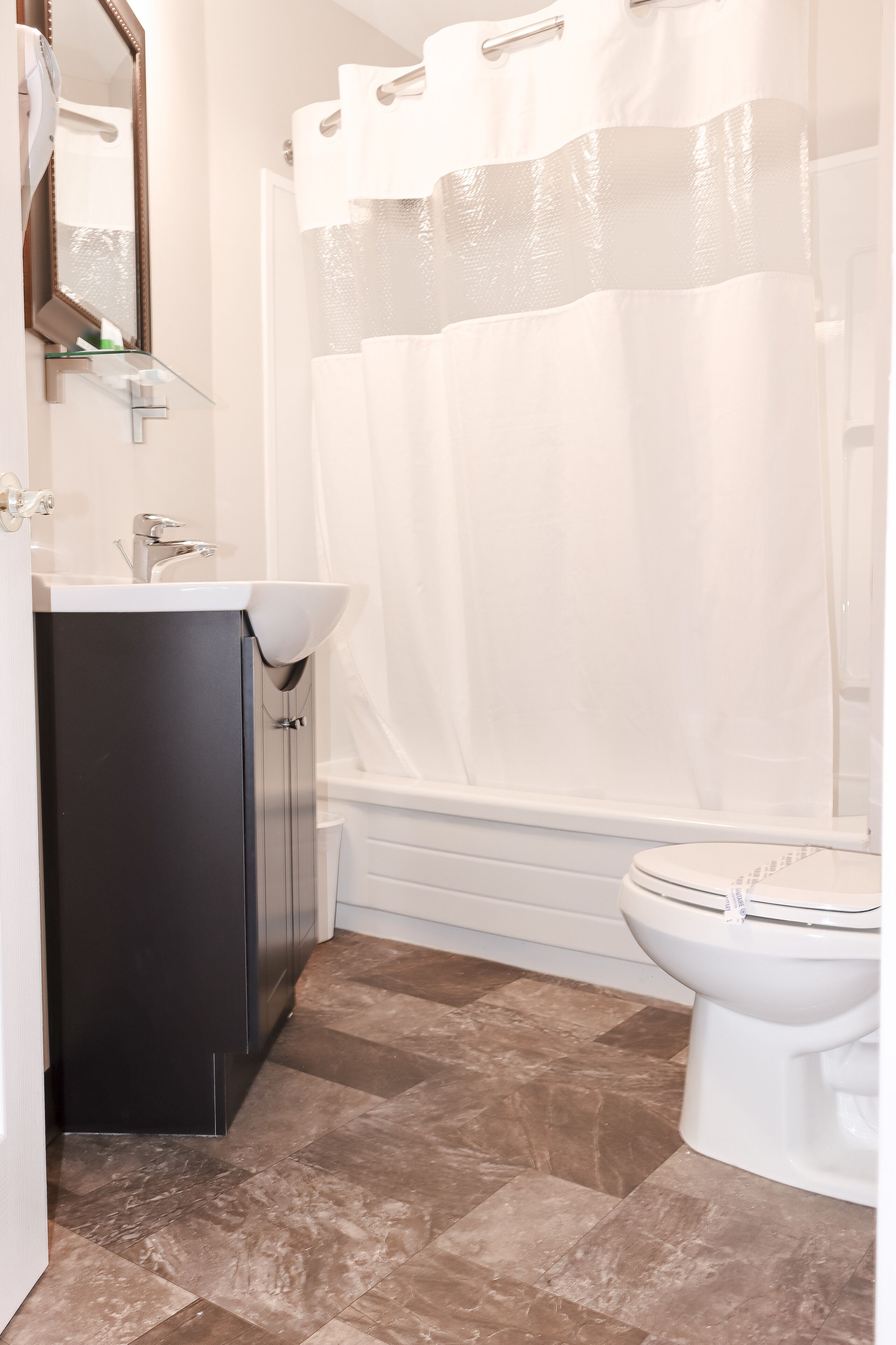 A bathroom with a white sink, dark cabinet, white toilet, and a shower curtain.