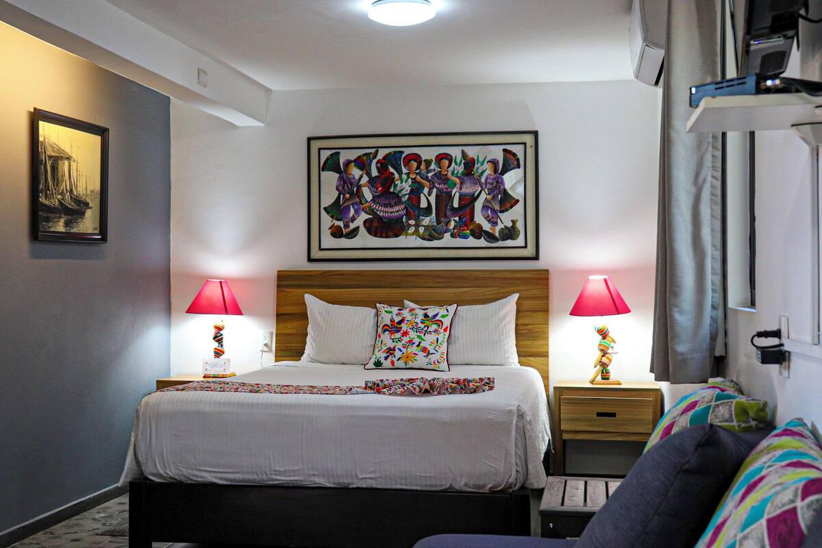 A hotel room with a large bed, two bedside lamps, a colorful artwork above the bed, and a framed picture on the wall.