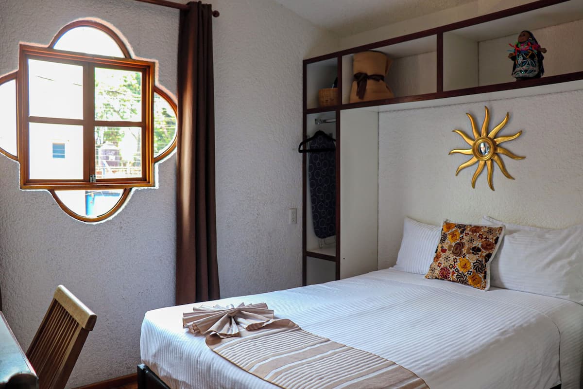 A bedroom with a bed, a chair, a window, and a shelf with items.