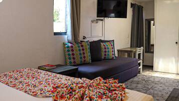 Quarto de hotel com cama, sofá, televisão fixada na parede e escrivaninha.