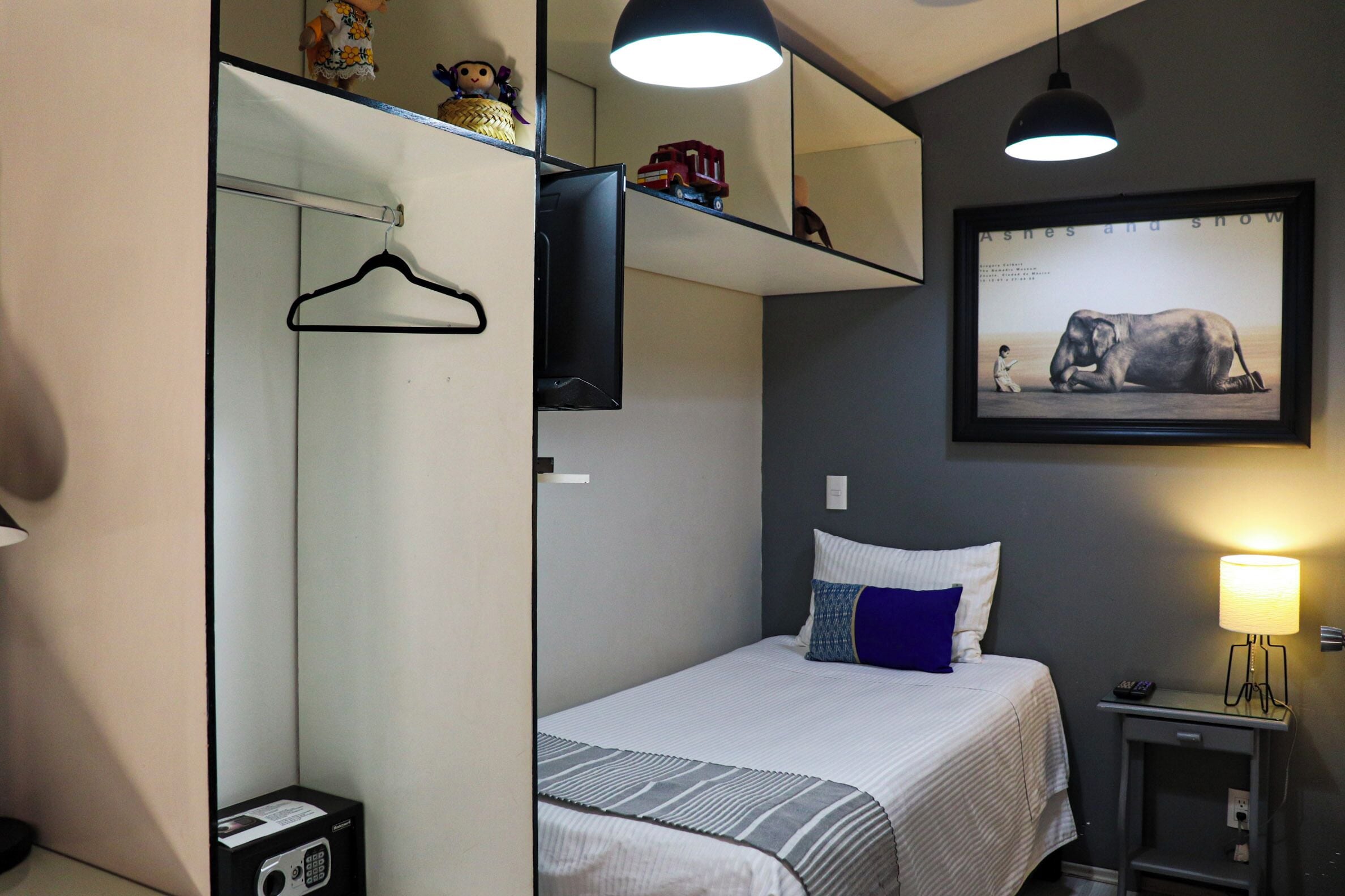 Ein Schlafzimmer mit Bett, Nachttisch, Lampe, gerahmtem Bild an der Wand und einer Garderobe.