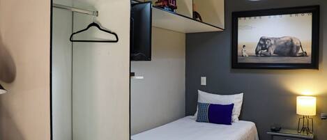Un dormitorio con cama, una mesita de noche, una lámpara, un cuadro en la pared y un perchero.