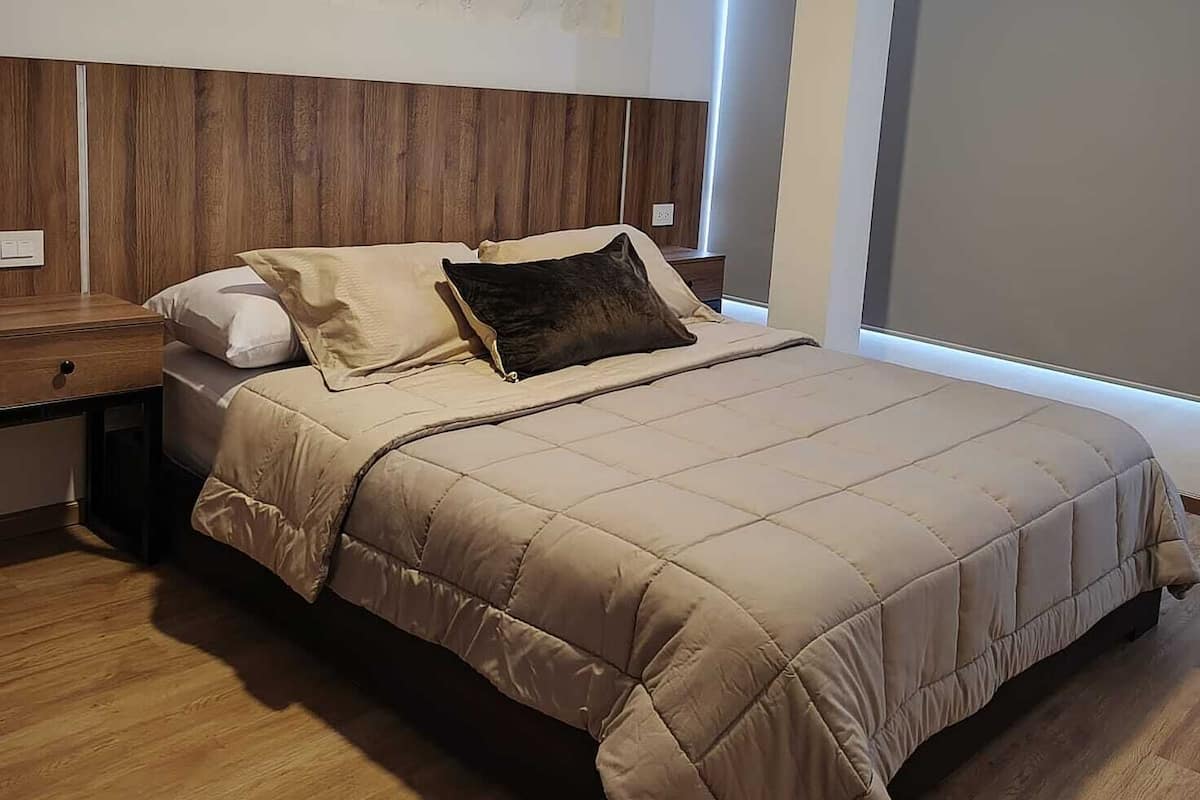 A bedroom with a bed, wooden headboard, bedside tables, and a large window.