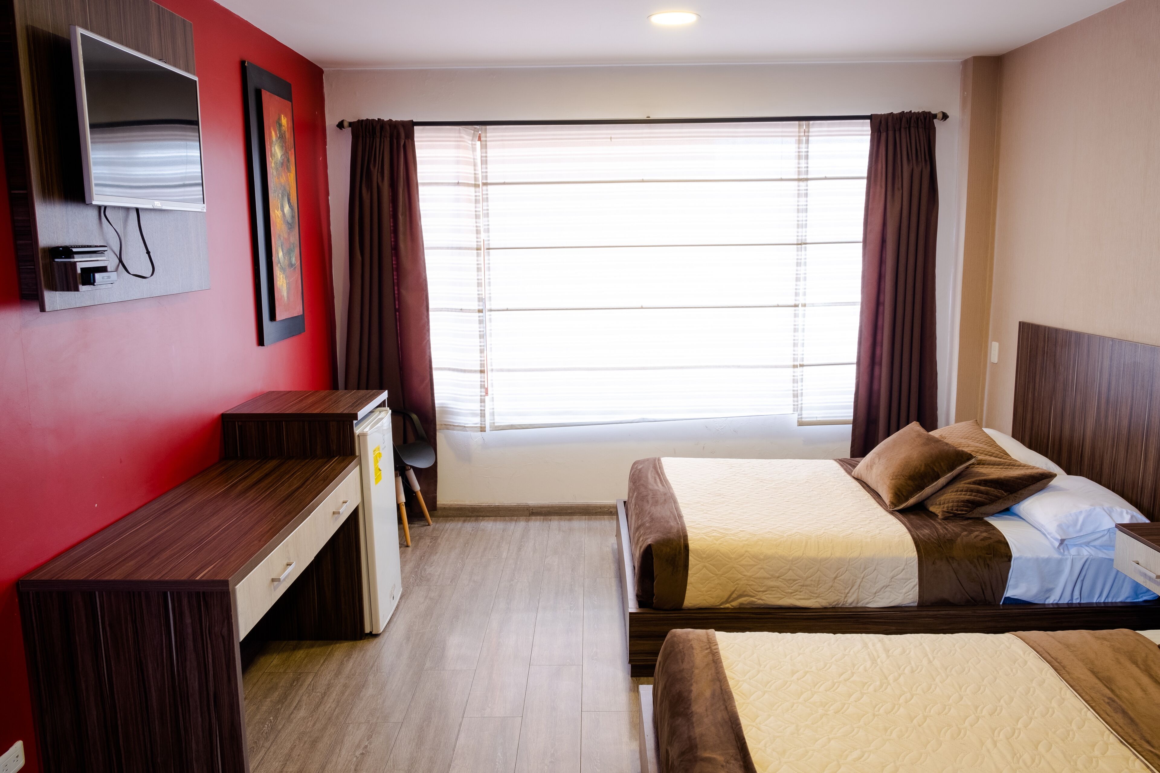 Habitación de hotel con dos camas, un escritorio, televisión y ventana con cortinas.