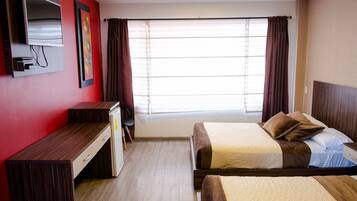 Habitación de hotel con dos camas, un escritorio, televisión y ventana con cortinas.