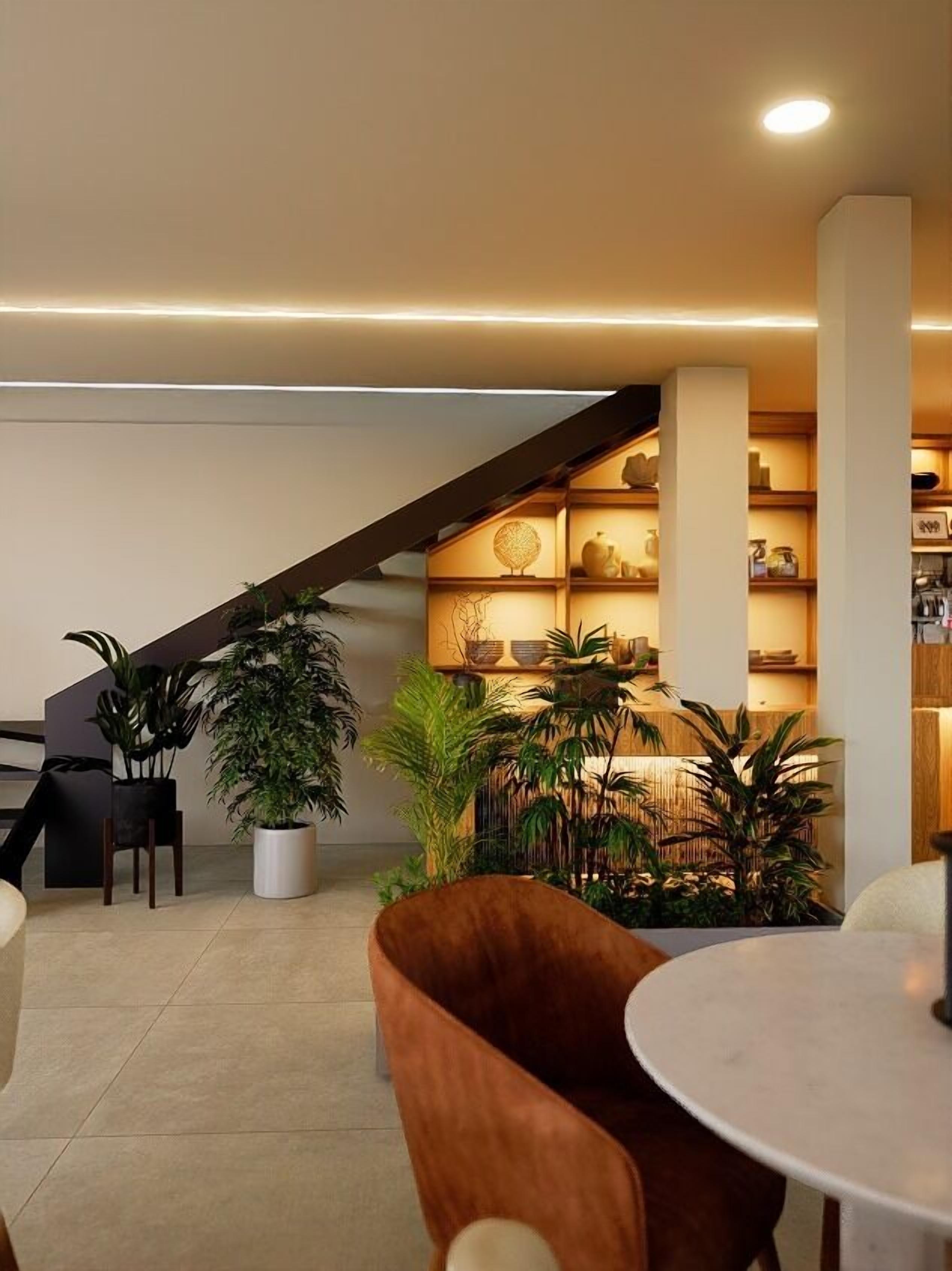 A modern interior with a staircase, seating area, and a plant-filled corner.