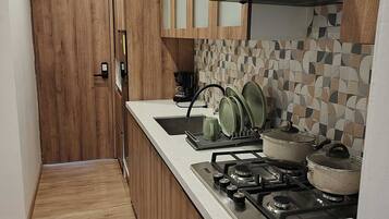 Une cuisine étroite avec des meubles en bois, un dosseret carrelé et une cuisinière à gaz avec des casseroles.