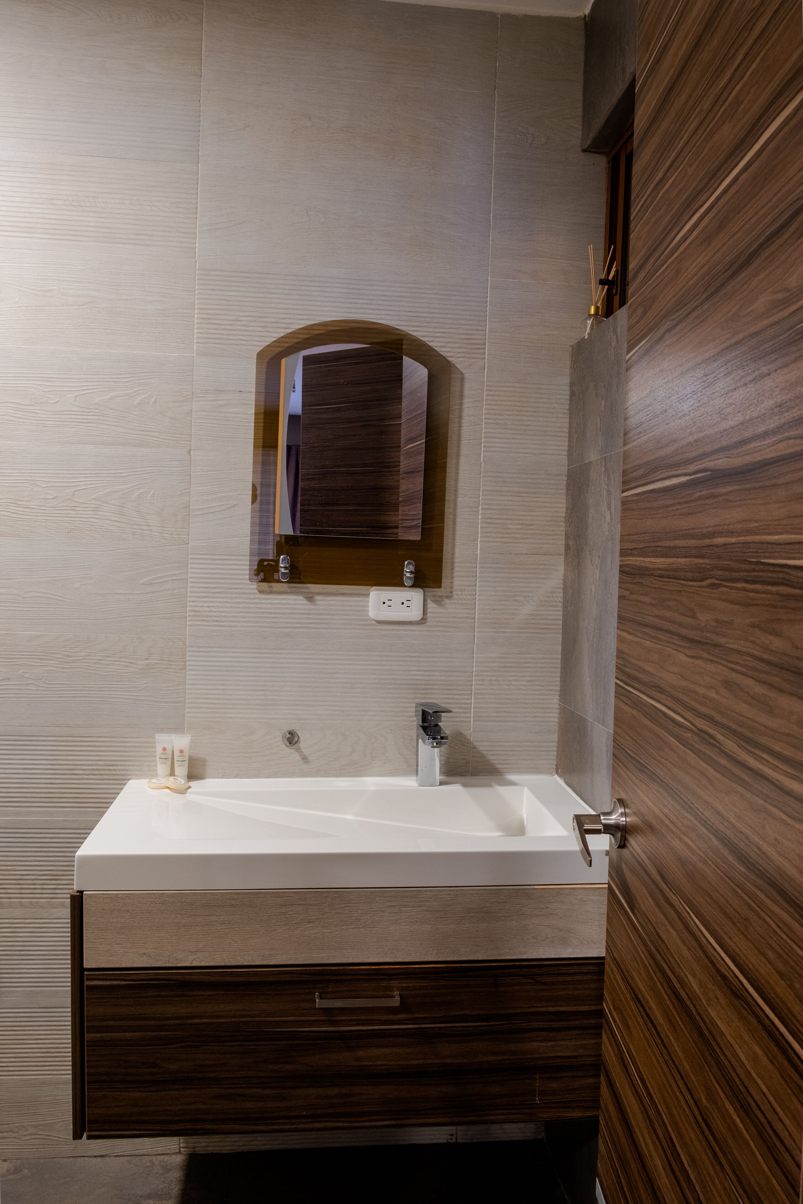 Een badkamer met een houten wastafelmeubel, een witte wasbak en een spiegel erboven.