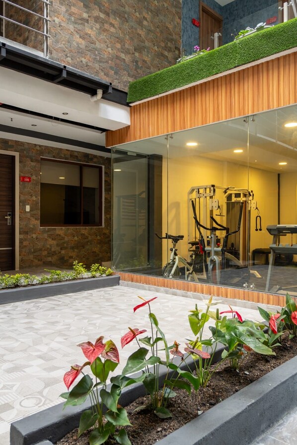 Un edificio moderno con fachada de piedra, un nivel superior de madera y una entrada de cristal que da a un espacio interior con equipo de ejercicio.