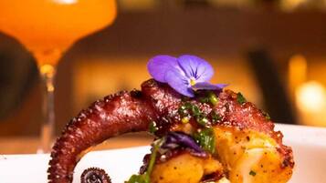 Een bord met octopus en een paarse bloem als garnering, samen met een glas oranje drank.