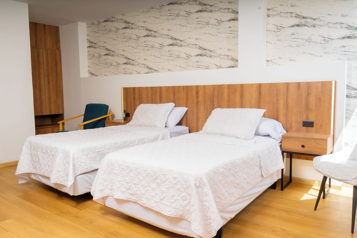 A hotel room with two single beds, a wooden headboard, a small wooden nightstand, a chair, and a marble-patterned wall.