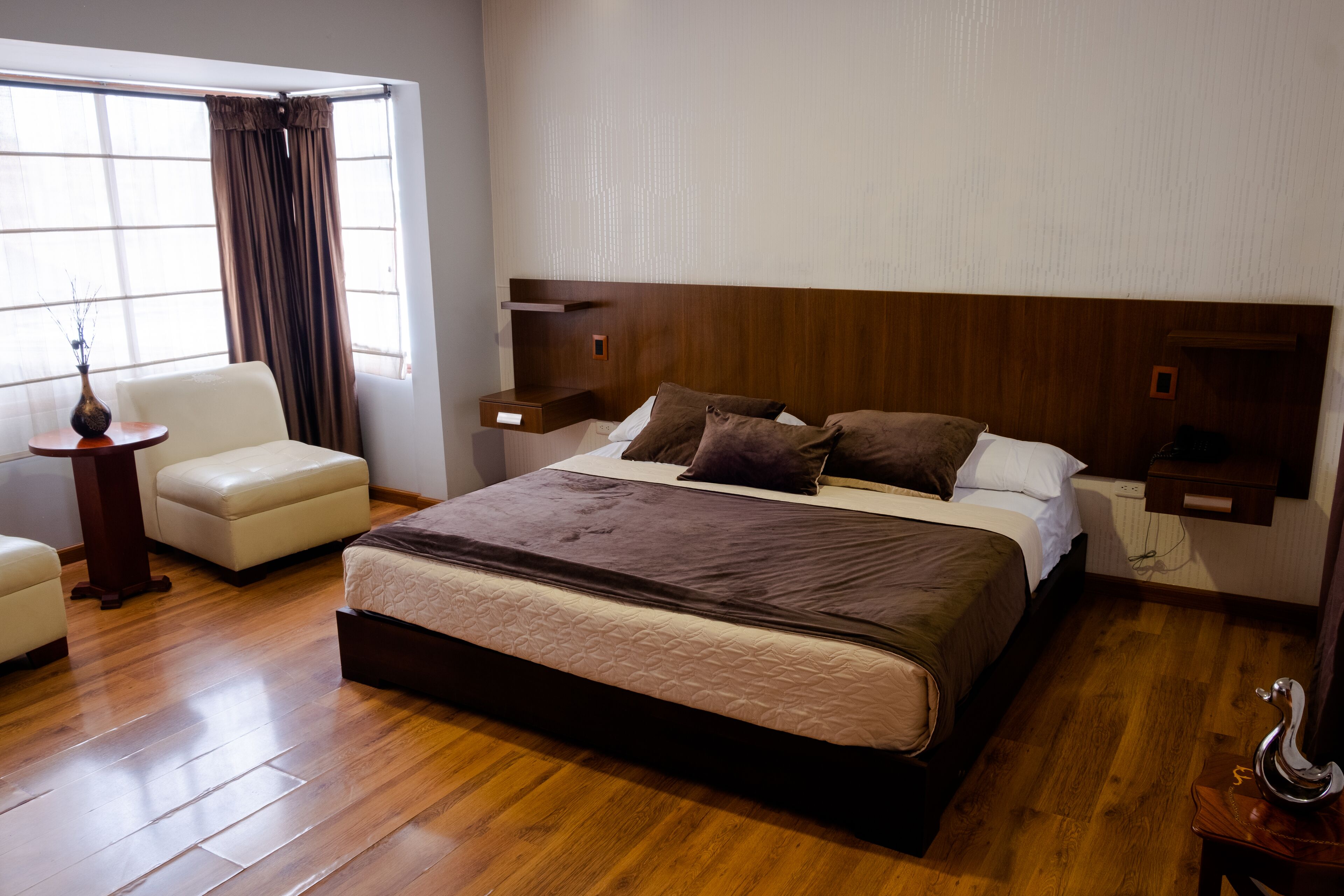 Une chambre à coucher avec un grand lit, une chaise, une table de chevet et une fenêtre avec des rideaux.